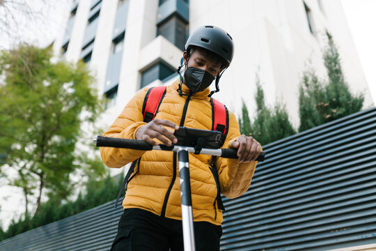 Male courier using mobile phone on kick scooter