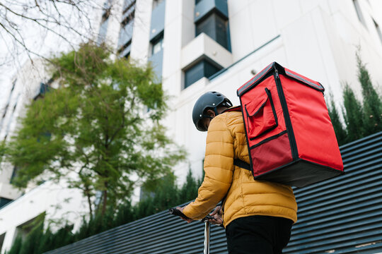 Male courier riding kick scooter and using cellphone