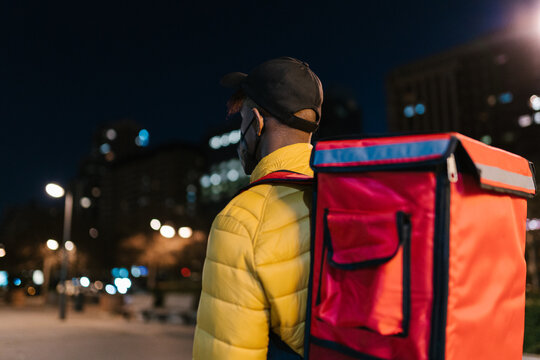 Anonymous delivery man with backpack carrying order in city