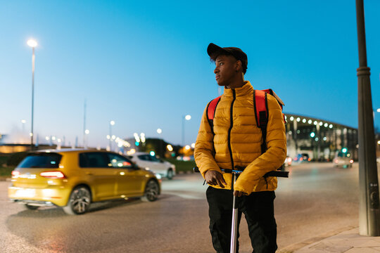 Black courier on kick scooter on sidewalk