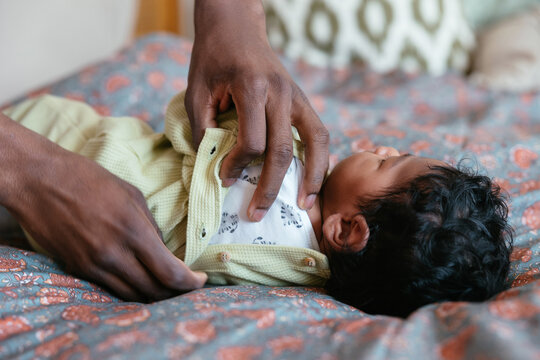 Crop parent dressing baby on bed