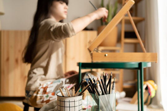 Artist girl painting picture on easel in living room