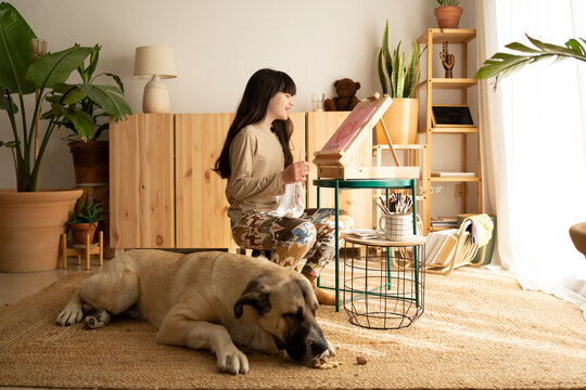 Girl drawing on wooden easel with her dog at home