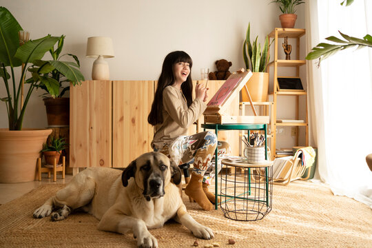 Girl painting on wooden easel with her dog at home