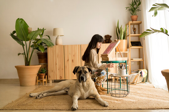 Girl drawing on easel with her dog at home