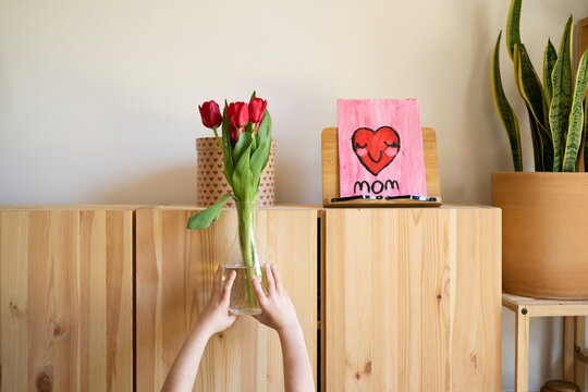 girl´s hand raising a flower vase to a tall cabinet  for mother's day