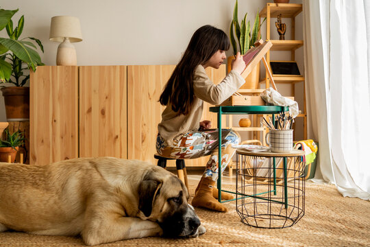 Girl drawing on tabletop easel with big dog at home 