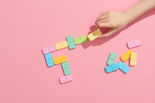 Girl plays dominoes. Domino closeup on a pink table background.