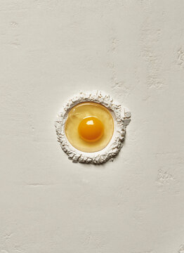 A crushed egg on a round bed of flour ready to be used for a cake