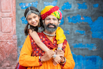 Portrait of happy indian father daughter hugging wearing traditional colorful rajasthani outfit looking at camera. rural india family. copy space