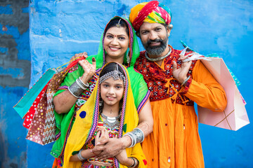 Portrait of happy traditional Indian family holding shopping bags against blue wall...