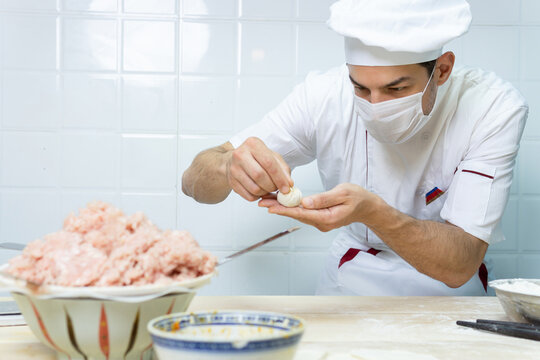 Male chef cook prepares dumplings and wearing face protective medical mask for protection from virus disease at restaurant kitchen.