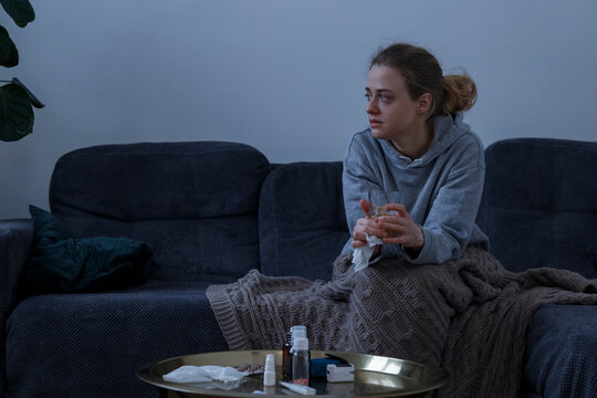 Sick woman with glass of tea on sofa at home