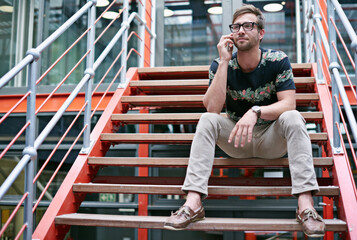Staying in touch with his clients. Shot of a handsome young man using his mobile phone while sitting on the steps of an office.
