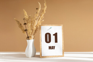 may 1. 1th day of month, calendar date.White vase with dried flowers on desktop in rays of sunlight on white-beige background. Concept of day of year, time planner, spring month - obrazy, fototapety, plakaty