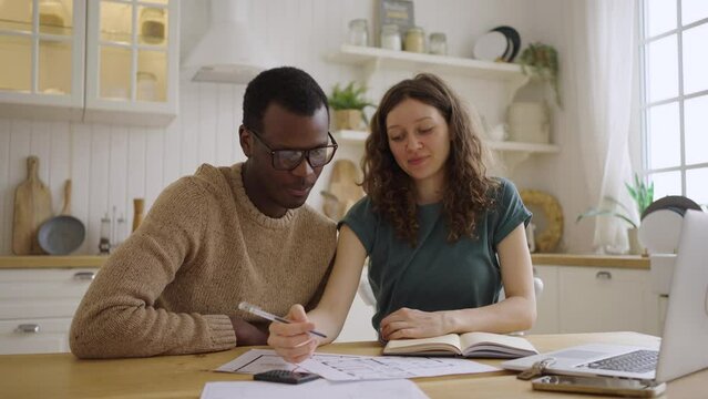 Happy white woman and African American realtor sign contract of apartment purchase. Man gives key to female buyer sitting at kitchen table