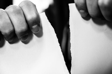 Two hands tearing a single blank sheet of paper from top to bottom. 
