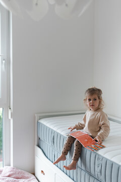 Toddler girl sitting on a double mattress in her bedroom at home