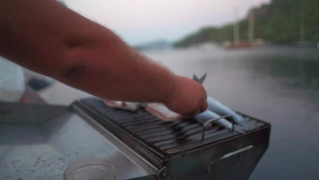 Small whole gutted fish are placed onto outdoor grill on moored yacht