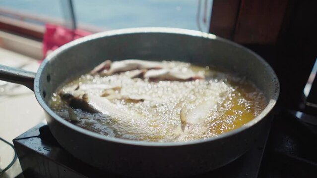 Slow motion: Small fish fry in sauce pan hot oil in ship's galley