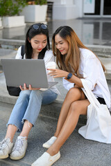 Two female college students sitting on stairs and looking something at laptop screen