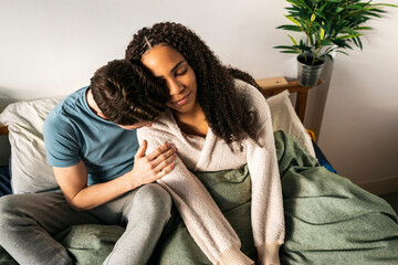 Diverse couple cuddling in bed enjoying day off at home