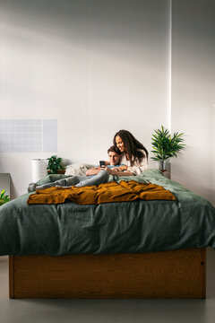 Multiracial couple browsing smartphone together on bed 
