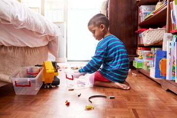 Playing and packing. Shot of a young boy sitting on the floor with toys in a bedroom.