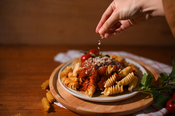 Female chef hands sprinkling Fusilli pasta with parmesan cheese.
