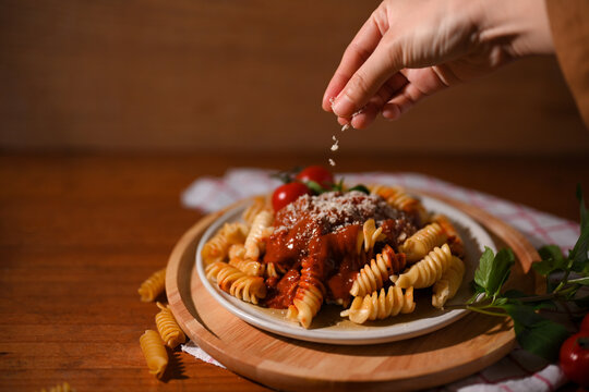 Female chef hands sprinkling Fusilli pasta with parmesan cheese.