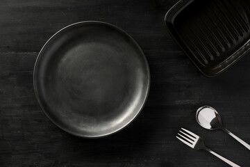 Empty black ceramic plate with silverware on black dining table background.