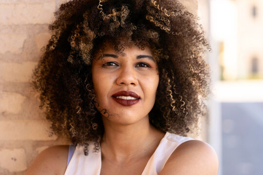 Charming woman with fluffy curl leaning on wall