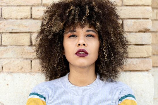 Confident woman with Afro hair near brick wall