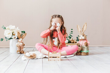 Little girl playing with Easter toy bunnies and a basket of Easter eggs. Child celebrating Easter. Easter egg hunt. Home decoration, bunnies and flowers