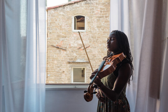 Black girl with viola by an open window