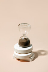 A side view of an hourglass with elapsed time sand, on a beige background with hard shadow copy...