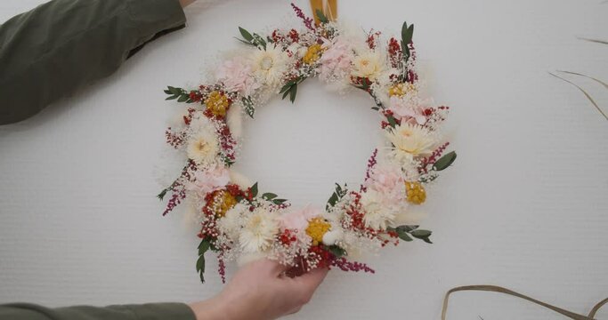 Florist puts wild flower crown on white wall, close up static view