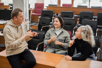Two girls and a guy are talking in sign language. Three deaf students chatting in a university...