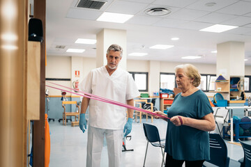 Aged patient exercising with elastic band near doctor