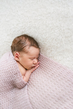 Newborn baby sleeping wrapped in a knit blanket.