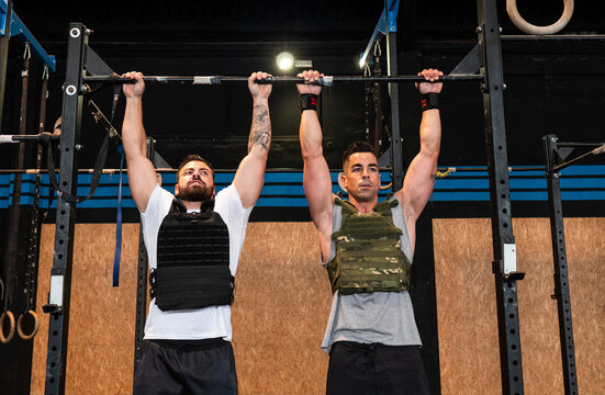 Powerful men doing pull ups in gym