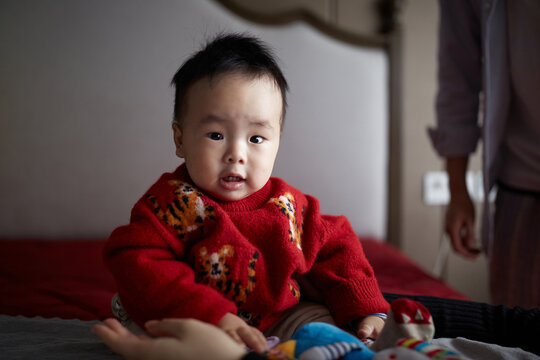 Cute Male Chinese Infant Sitting On A Bed At Home In Anhui, China.