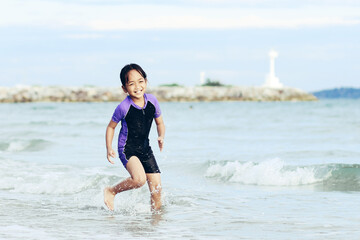 little Asian girl running and playing with smiling and laughing on tropical beach at sunset. Portrait of Adorable young child kids having fun in summer holiday vacation travel.