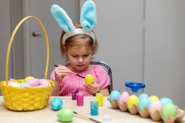 Little girl in Easter bunny ears painting colored eggs. Easter family holiday celebration at home and craft concept.