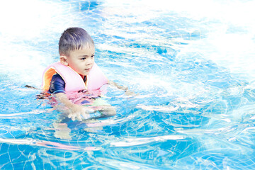 Fototapeta na wymiar Cute boy wearing safety inflatable armbands swimming in swimming pool