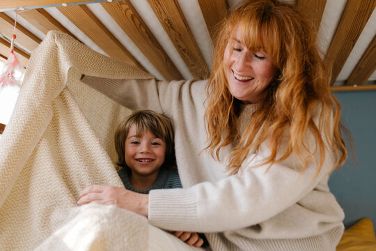 A little boy is hiding under a blanket in a bed