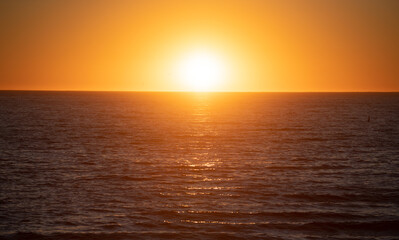Fototapeta premium Sunset with large yellow sun under the sea surface. Calm ocean with sunset sky and sun through the clouds over. Calm ocean and sky background.
