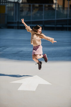 Young girl jumps over a painted arrow on the pavement. 
