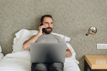 Male worker using laptop and talking on smartphone