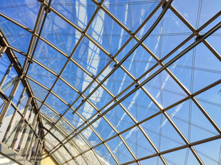 Gitterstrukturen eines Glasdaches mit blauem Himmel im Hintergrund.